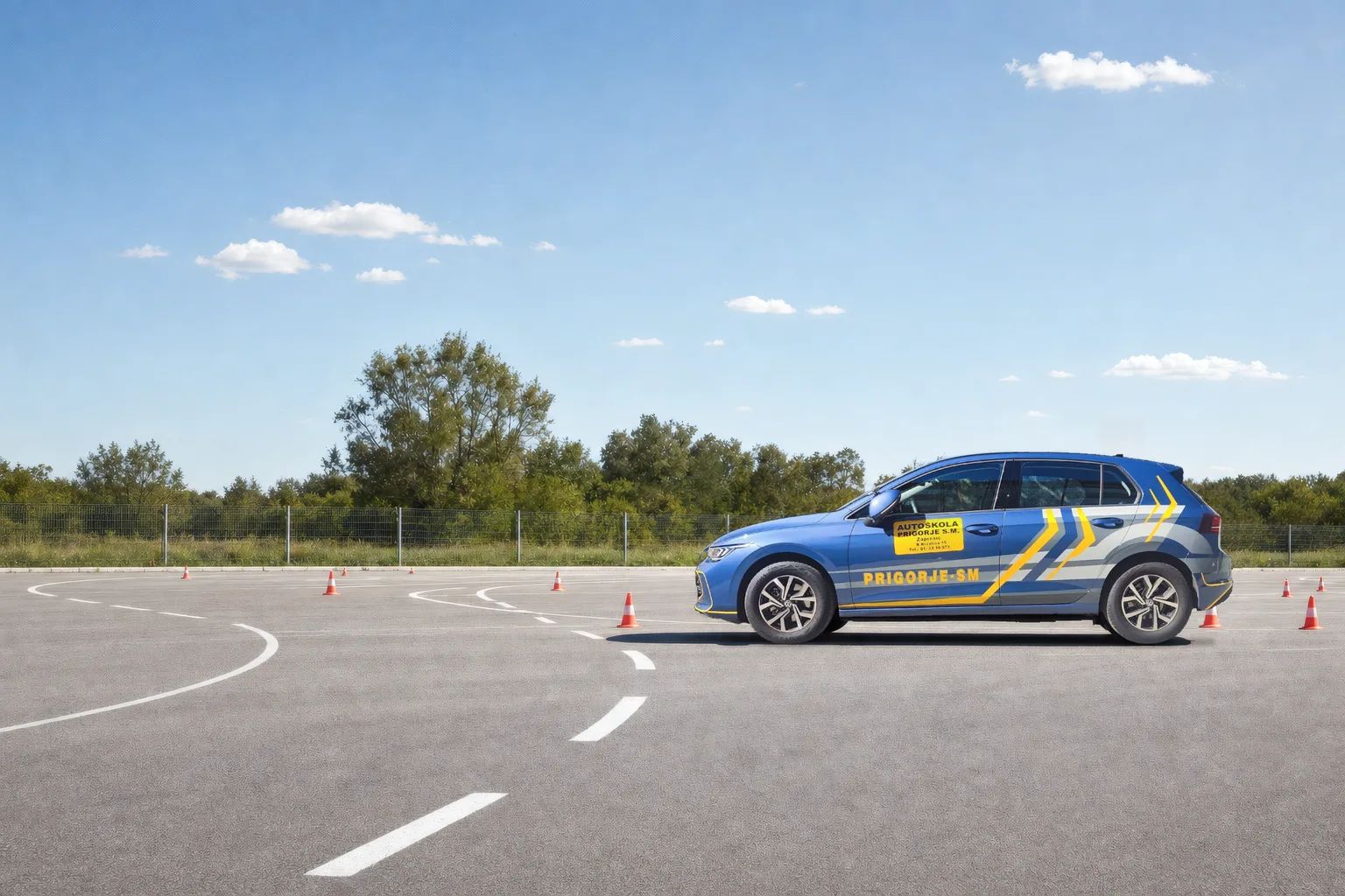 Plavi automobil Autoškole Prigorje S.M. s natpisom PRIGORJE-SM iz profila na sunčanom vježbalištu, između narančastih čunjeva i bijelih oznaka na asfaltu
