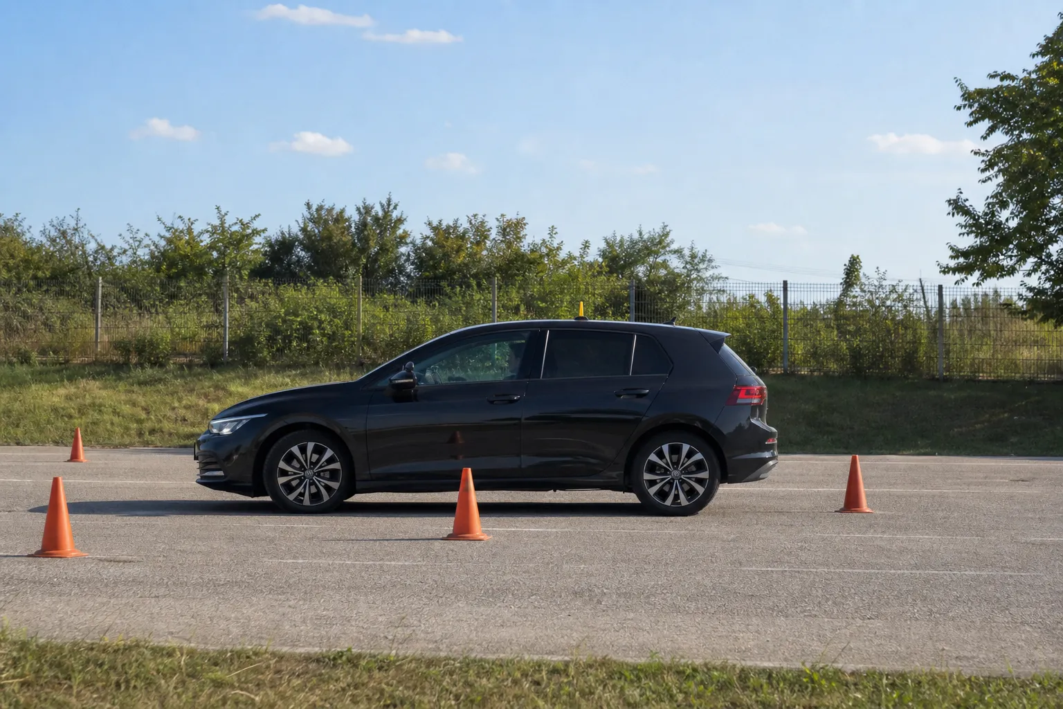 Automobil autoškole iz profila vozi slalom između čunjeva na sunčanom vježbalištu